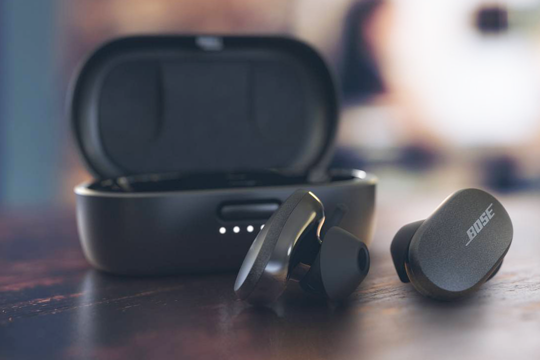 Black QuietComfort earbuds sitting outside of their charging case on a dark wood table