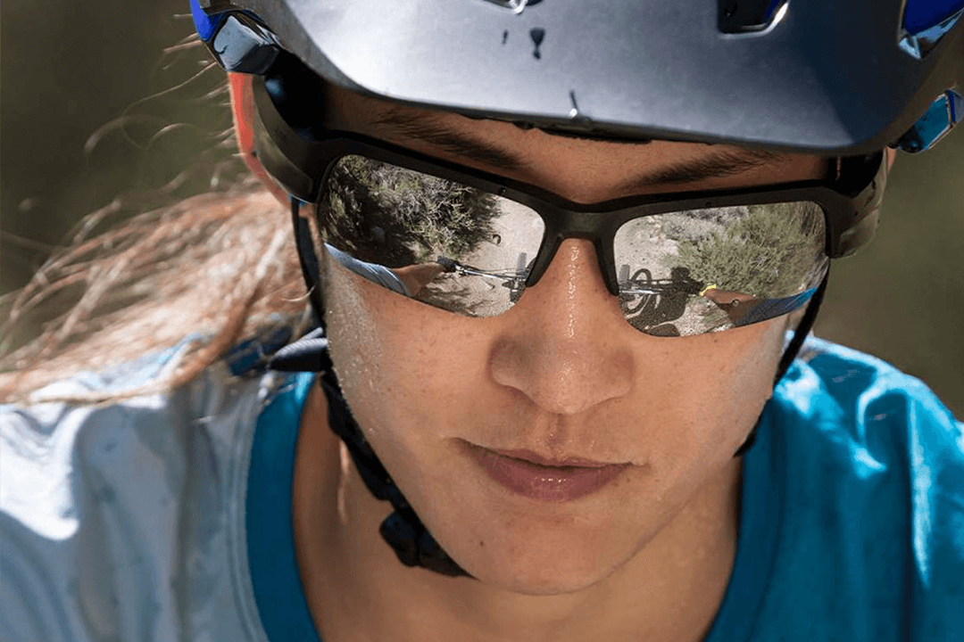 White woman wearing Bose Frames Tempo with silver lenses. Her helmet implies that she is biking. 